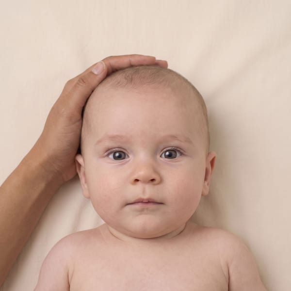 Baby with an adult's hand supporting the head, visible in the frame