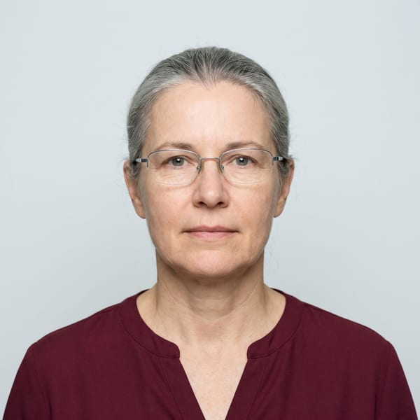 Woman with grey hair and thin silver glasses against a plain pale background
