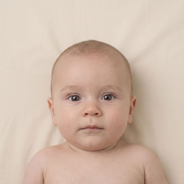 Baby photographed from above on a plain sheet, eyes open