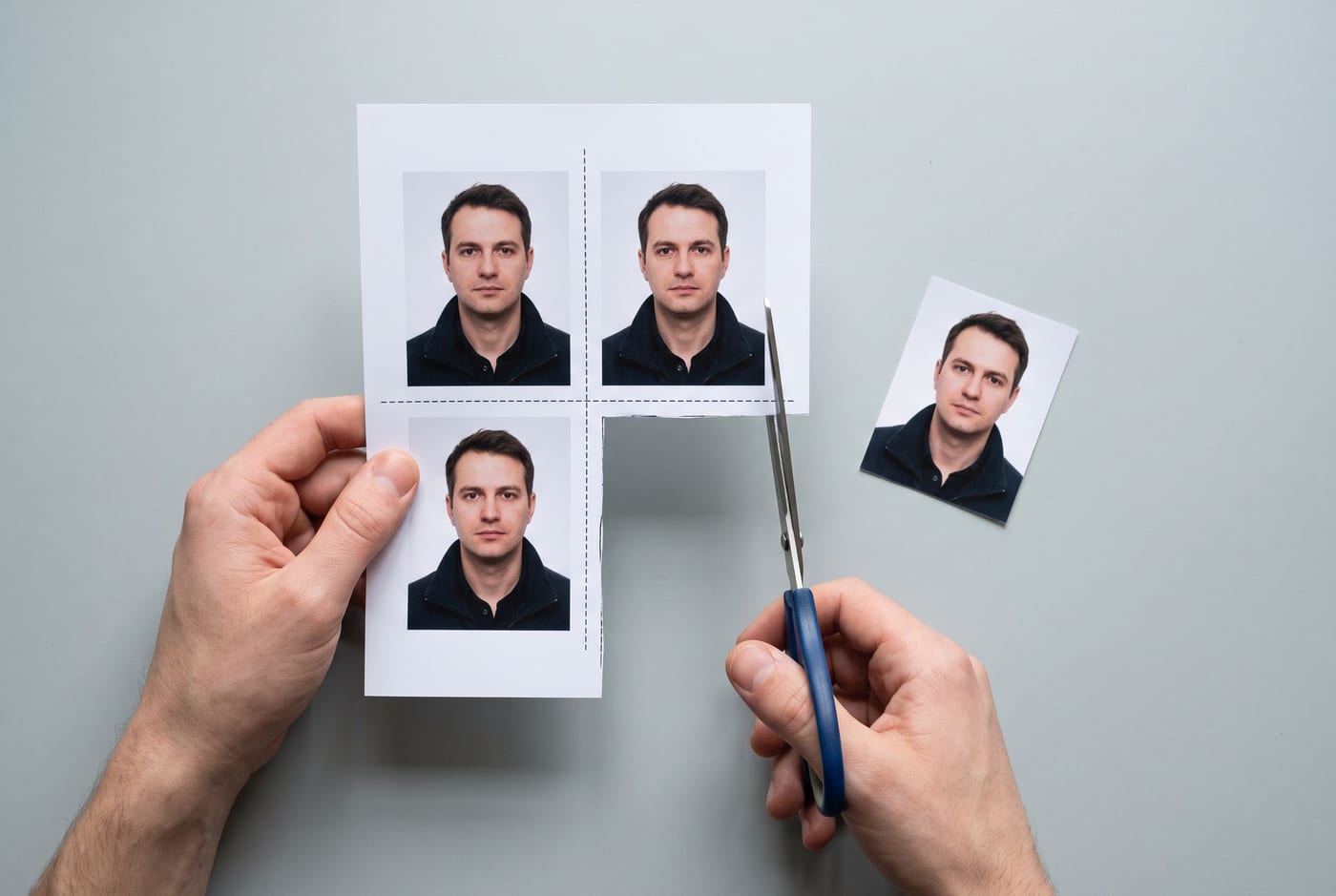 Hands cutting a printed photo sheet along its dashed guide lines with scissors